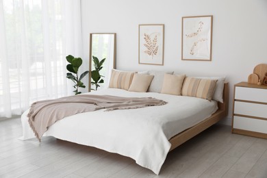 Photo of Large bed, houseplant and full-length mirror near window in room. Stylish bedroom interior