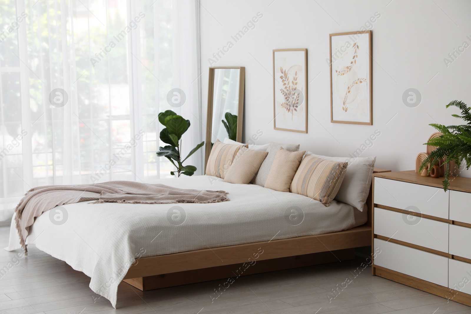 Photo of Large bed, houseplant and full-length mirror near window in room. Stylish bedroom interior