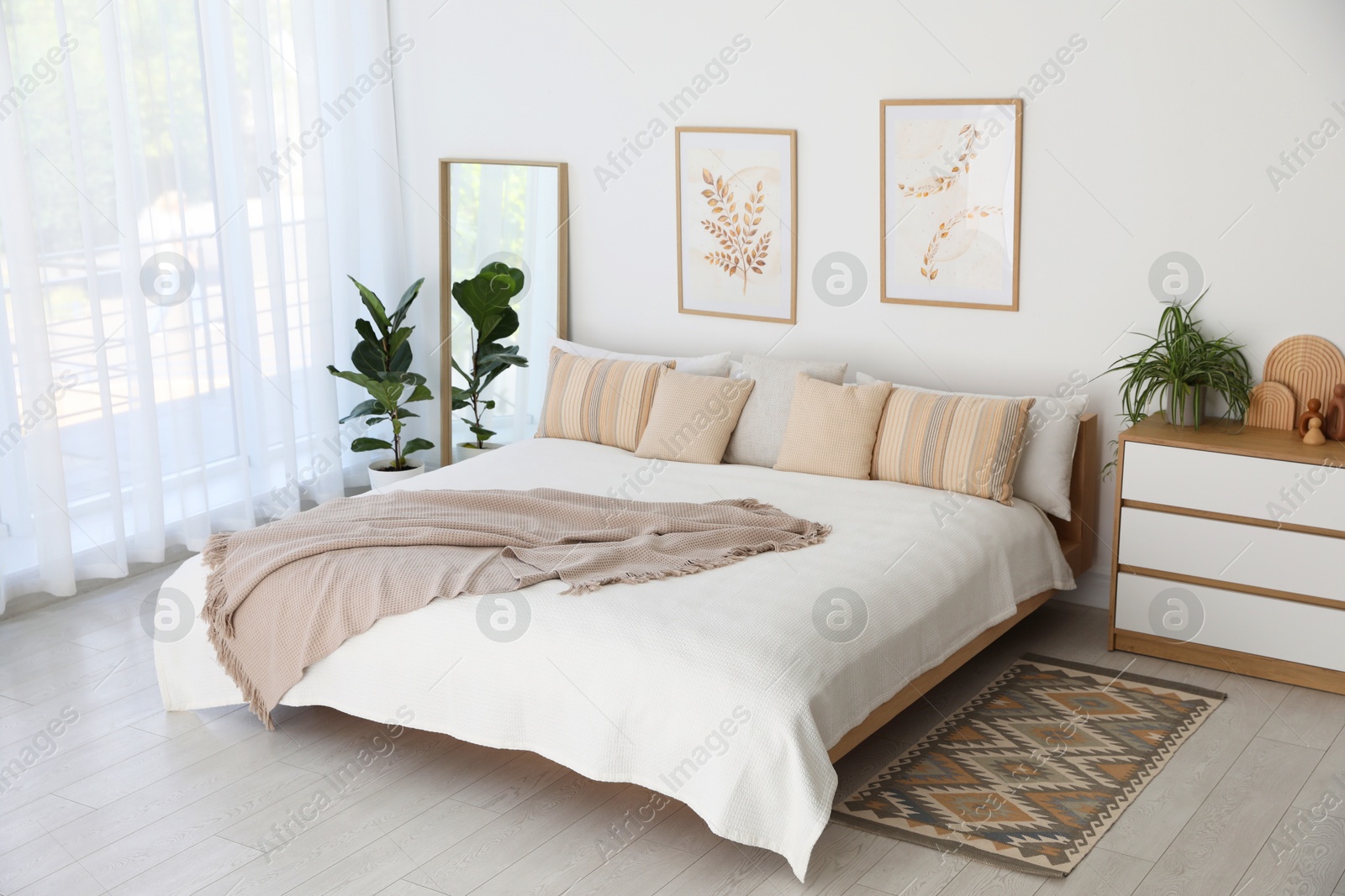 Photo of Large bed, houseplant and full-length mirror near window in room. Stylish bedroom interior