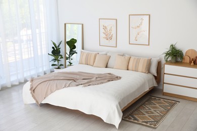 Photo of Large bed, houseplant and full-length mirror near window in room. Stylish bedroom interior