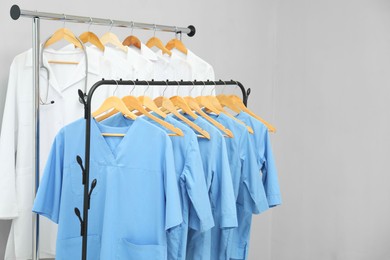 Photo of Different medical workers' uniforms on clothing racks against grey background. Space for text