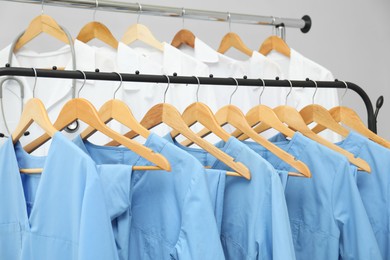 Photo of Different medical workers' uniforms on clothing racks against grey background, closeup