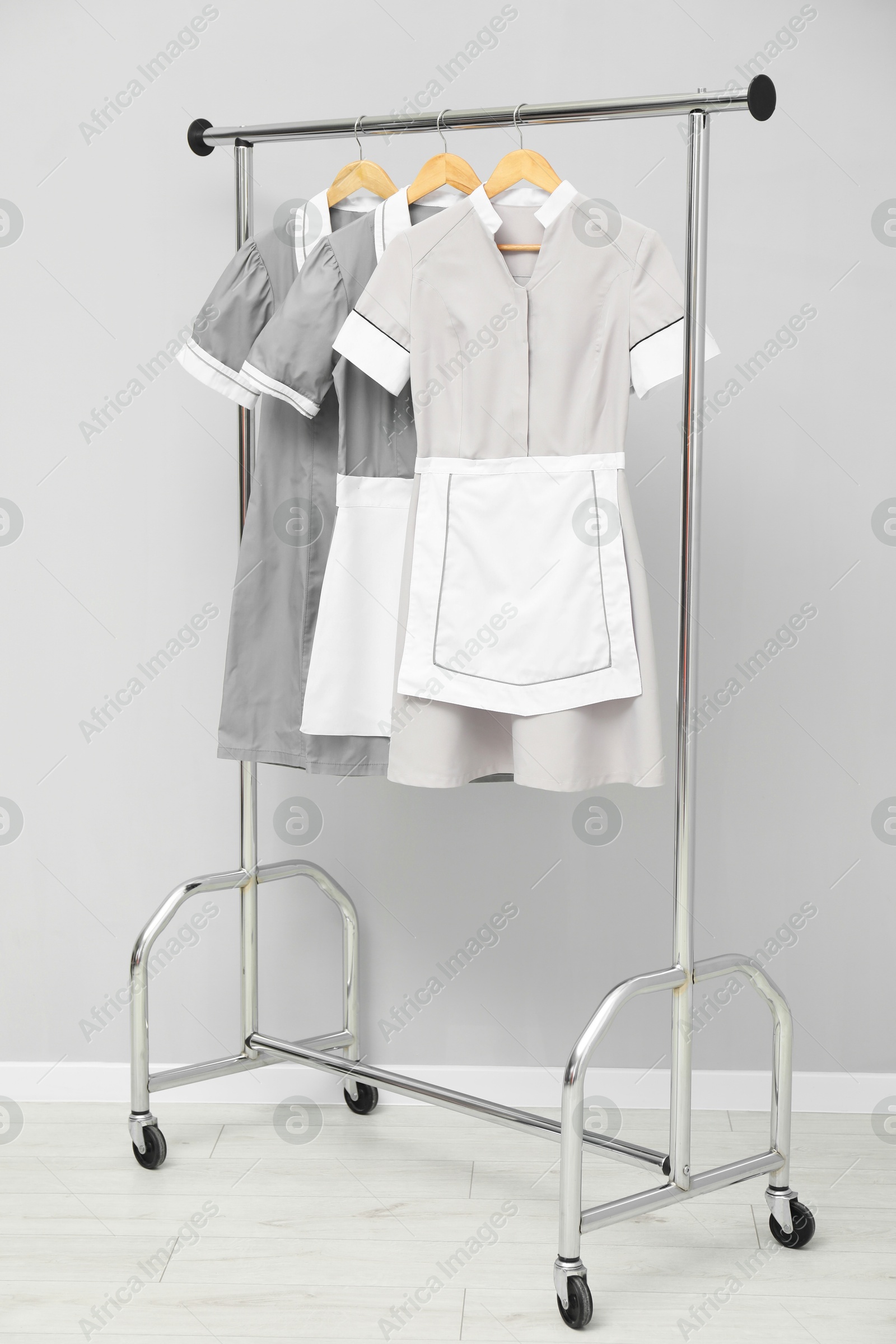 Photo of Maids' uniforms on clothing rack near grey wall indoors