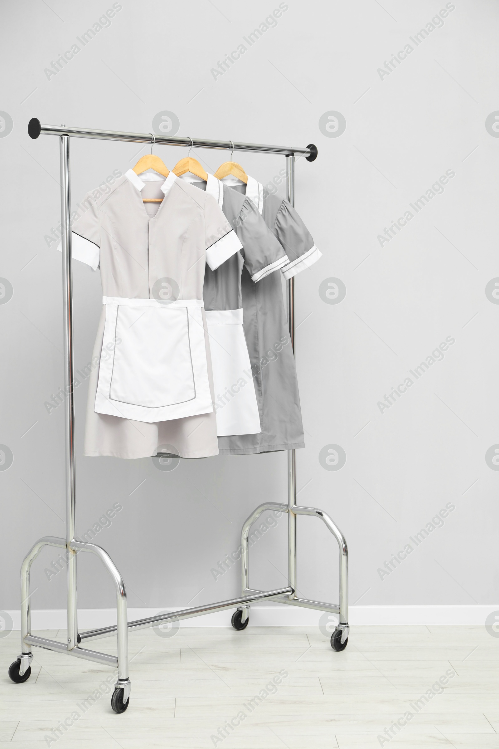 Photo of Maids' uniforms on clothing rack near grey wall indoors