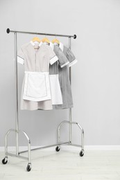 Photo of Maids' uniforms on clothing rack near grey wall indoors