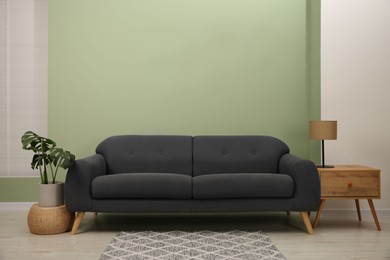 Photo of Stylish sofa, side table and houseplant near green wall indoors