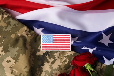 Photo of Veterans day. USA army patch, rose flowers and military uniform on American flag, flat lay