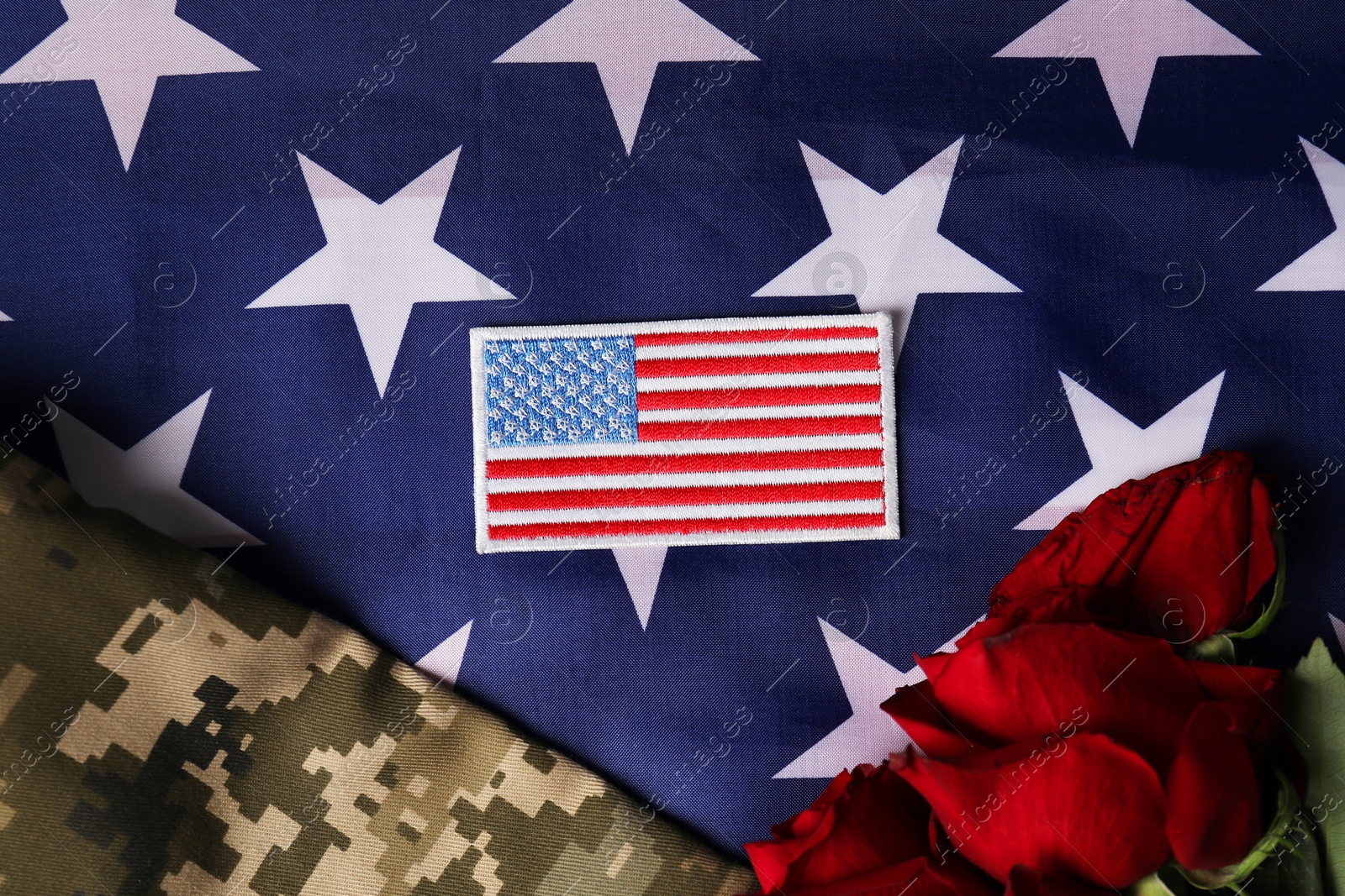 Photo of Veterans day. USA army patch, rose flowers and military uniform on American flag, flat lay