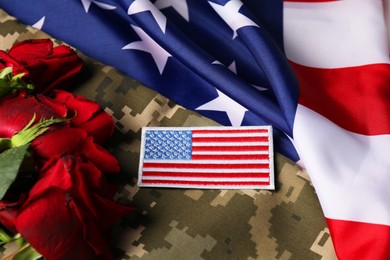 Photo of Veterans day. USA army patch, rose flowers and military uniform on American flag, above view