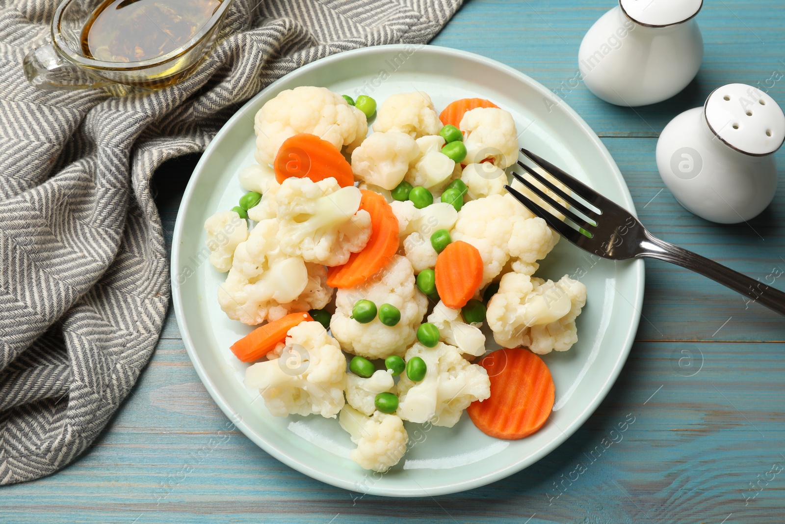 Photo of Tasty cooked cauliflower with green peas and carrot slices served on light blue wooden table, flat lay