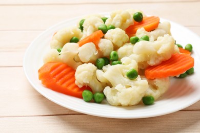 Photo of Tasty cooked cauliflower with green peas and carrot slices on white wooden table, closeup