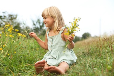 Photo of Barefoot little girl with flowers at meadow. Child enjoying beautiful nature