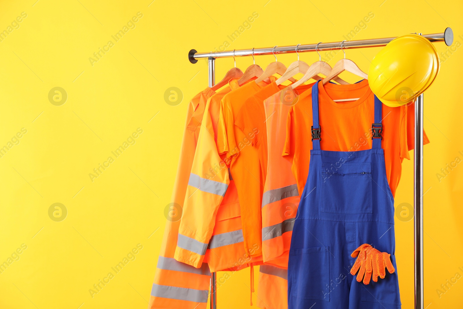 Photo of Workers' uniforms on clothing rack against yellow background. Space for text