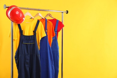 Photo of Workers' uniforms on clothing rack against yellow background. Space for text