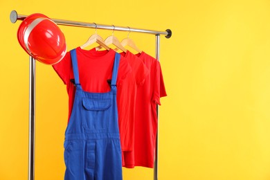 Photo of Workers' uniform and t-shirts on clothing rack against yellow background. Space for text