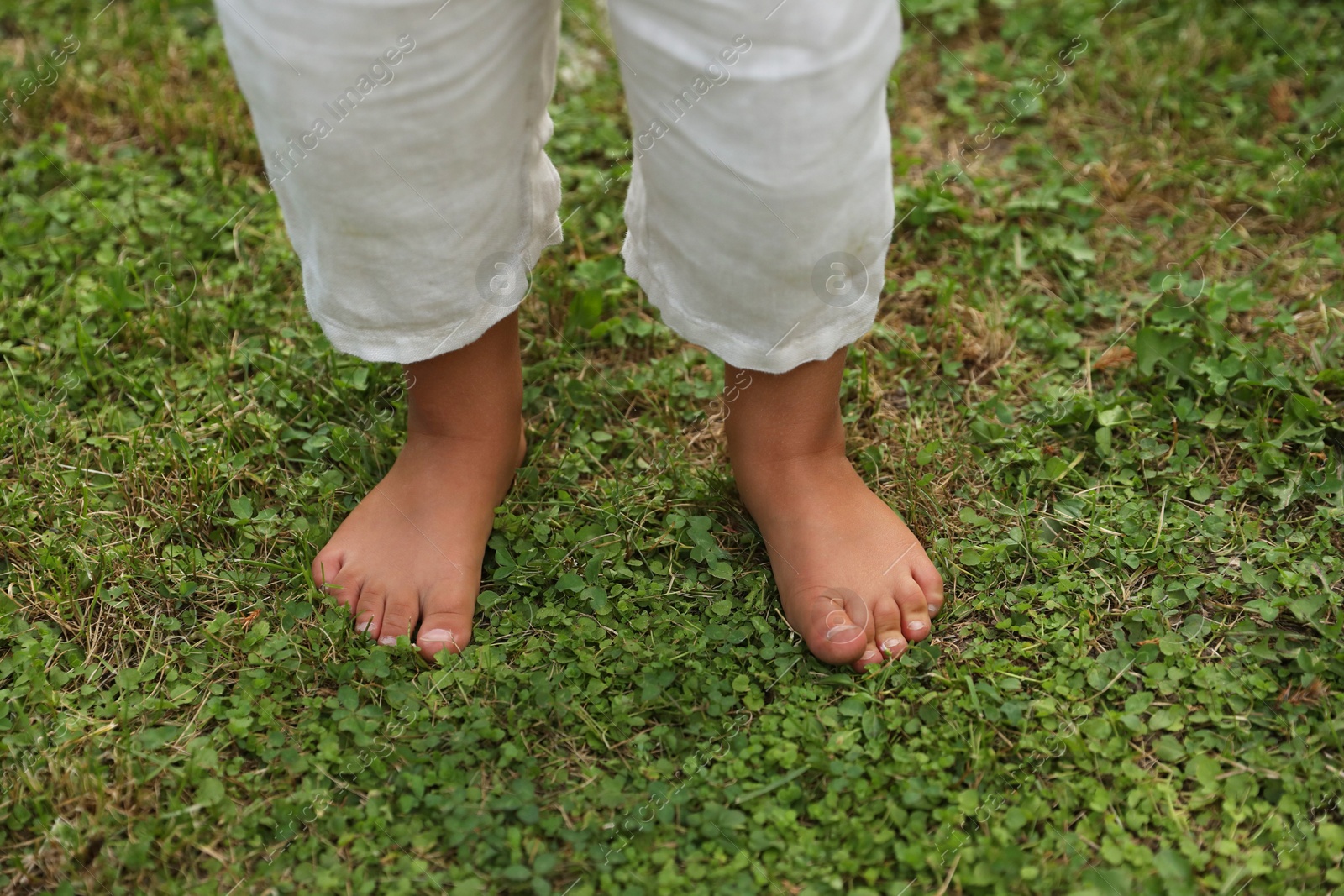 Photo of Little child standing barefoot on green grass outdoors, closeup. Enjoying nature