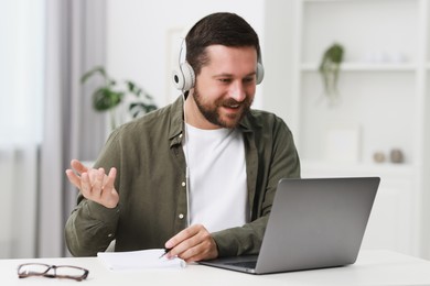 Interpreter in headphones having video chat via laptop at white table indoors