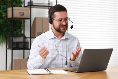 Interpreter in headset having video chat via laptop at wooden table indoors