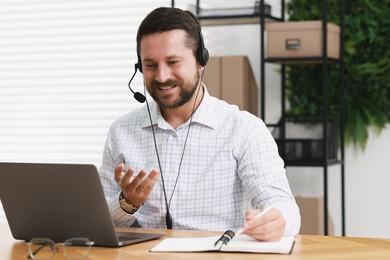 Interpreter in headset taking notes while having video chat via laptop at wooden table indoors