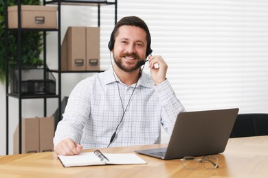 Interpreter in headset having video chat via laptop at wooden table indoors