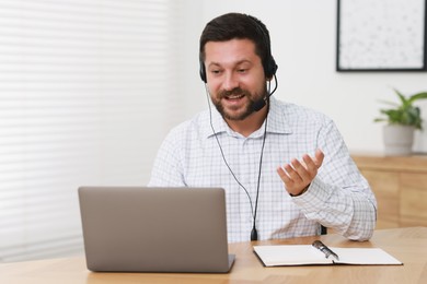 Interpreter in headset having video chat via laptop at wooden table indoors