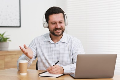 Photo of Interpreter in headphones having video chat via laptop at wooden table indoors