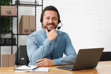 Interpreter in headset having video chat via laptop at wooden table indoors