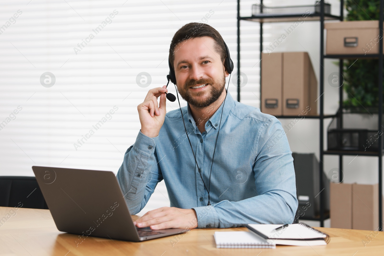 Photo of Interpreter in headset having video chat via laptop at wooden table indoors