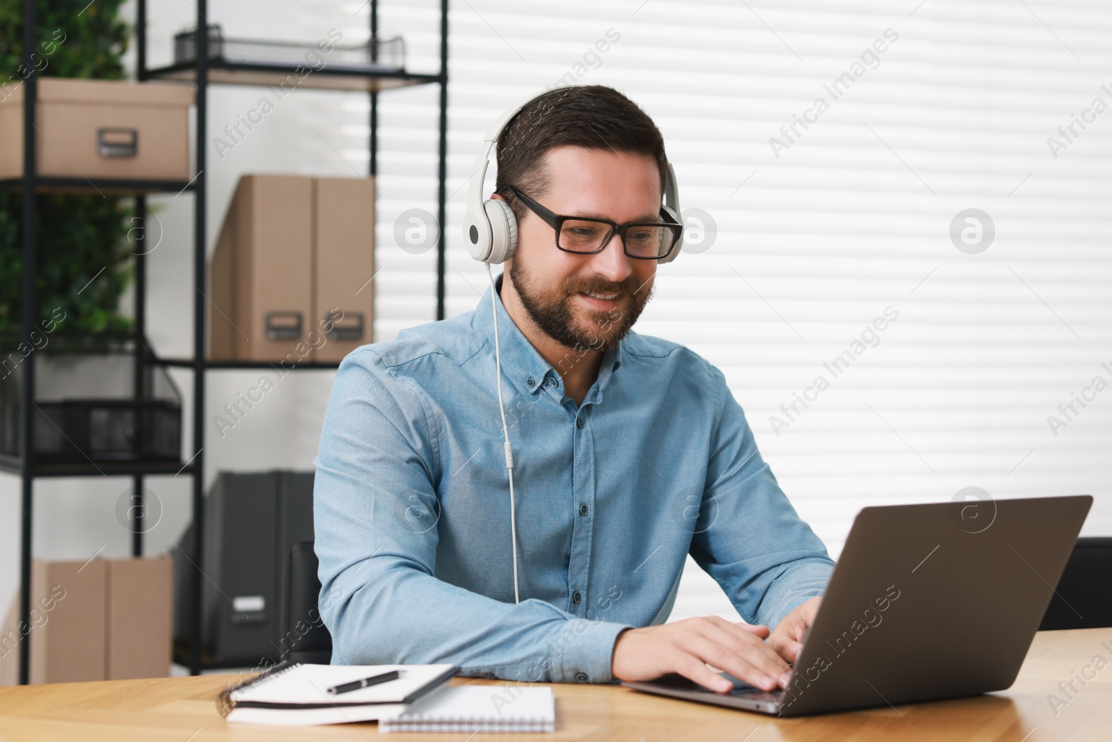 Photo of Interpreter in headphones having video chat via laptop at wooden table indoors