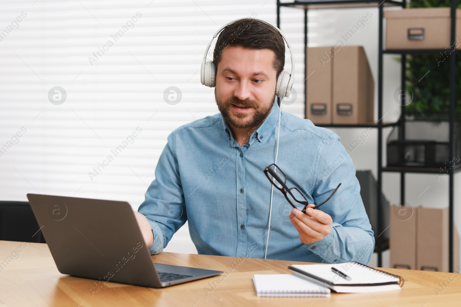 Photo of Interpreter in headphones having video chat via laptop at wooden table indoors