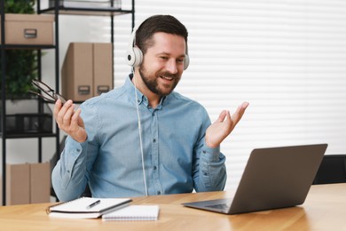 Interpreter in headphones having video chat via laptop at wooden table indoors