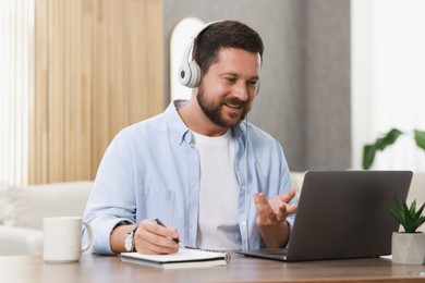 Photo of Interpreter in headphones having video chat via laptop at wooden table indoors