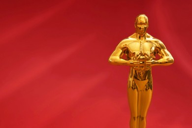 Photo of Golden trophy in shape of human figure on red background, closeup. Space for text