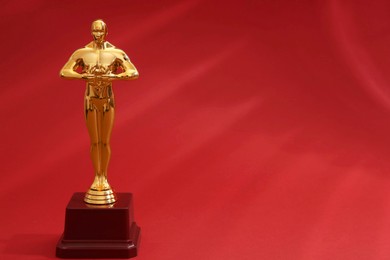 Golden trophy in shape of human figure on red background, space for text