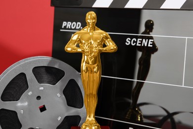 Photo of Golden trophy in shape of human figure, movie clapper and film reel on red background, closeup