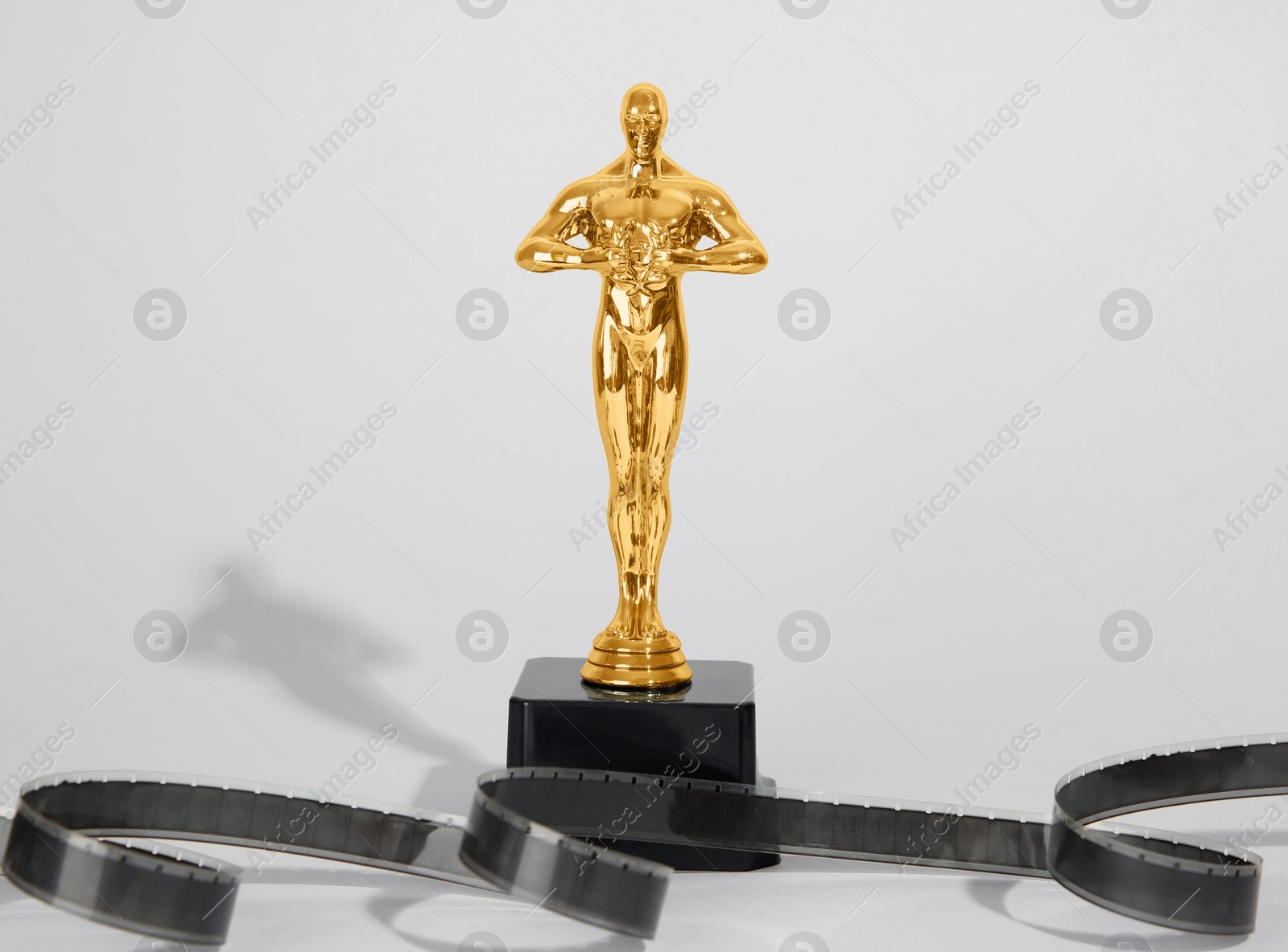 Photo of Golden trophy in shape of human figure and film reel on light background