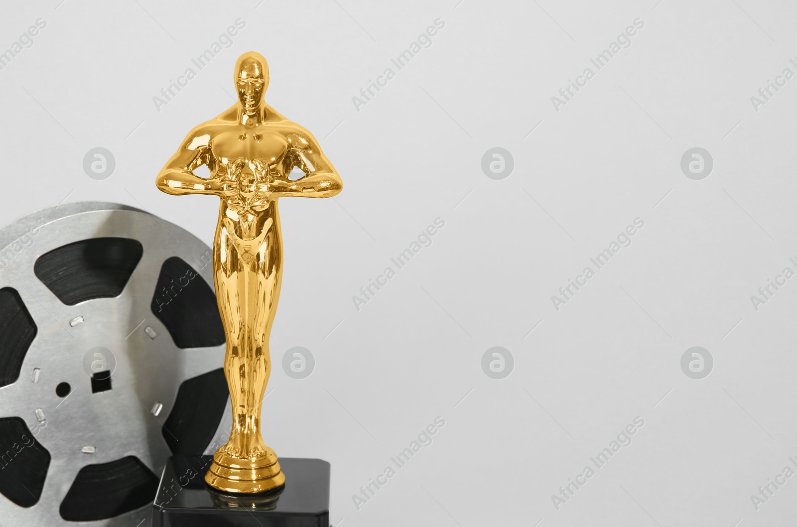 Photo of Golden trophy in shape of human figure and film reel on light background, space for text