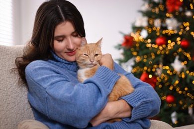 Photo of Woman with cute ginger cat in room decorated for Christmas