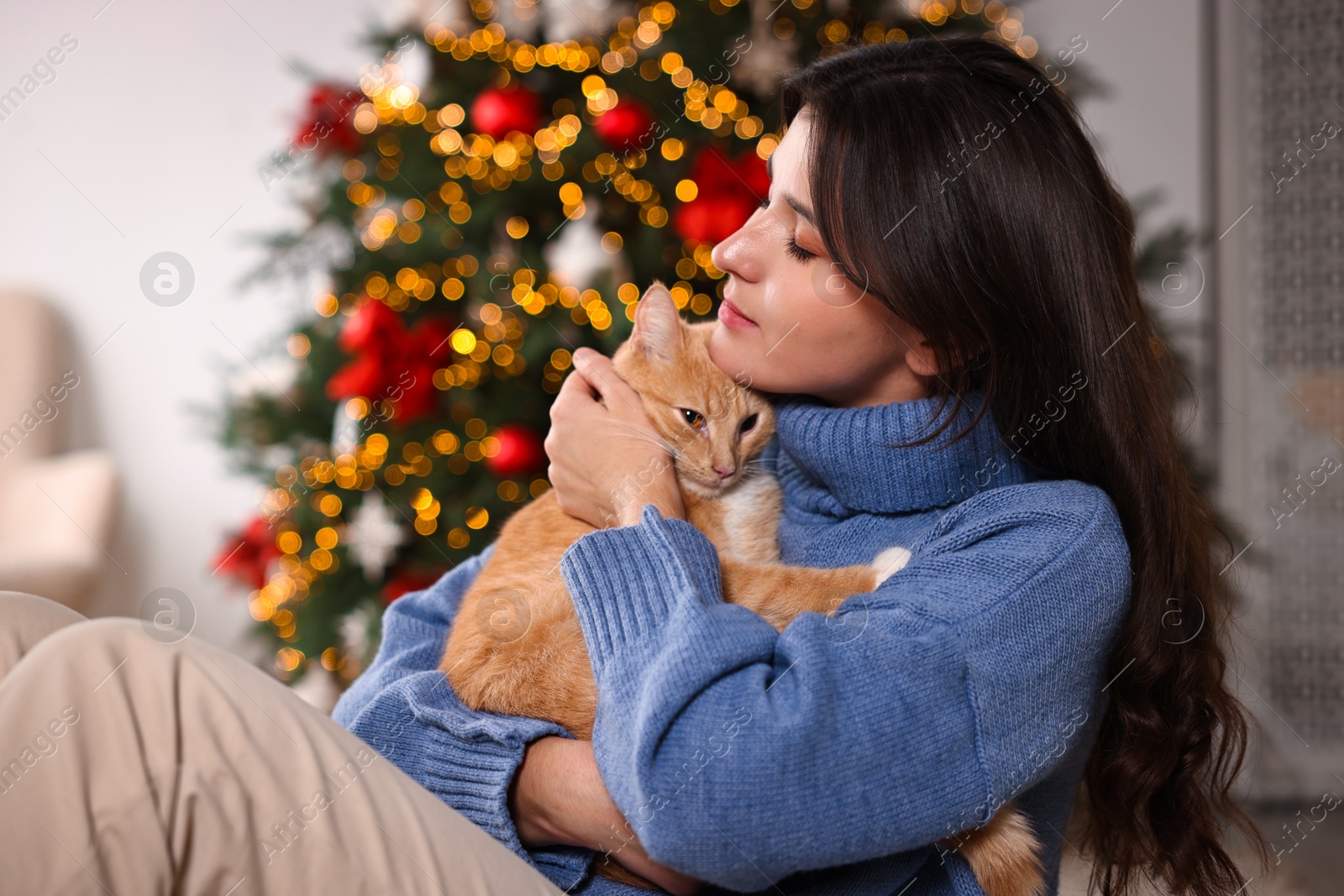 Photo of Woman with cute ginger cat in room decorated for Christmas