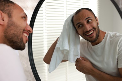 Photo of Smiling man with towel looking at mirror in bathroom