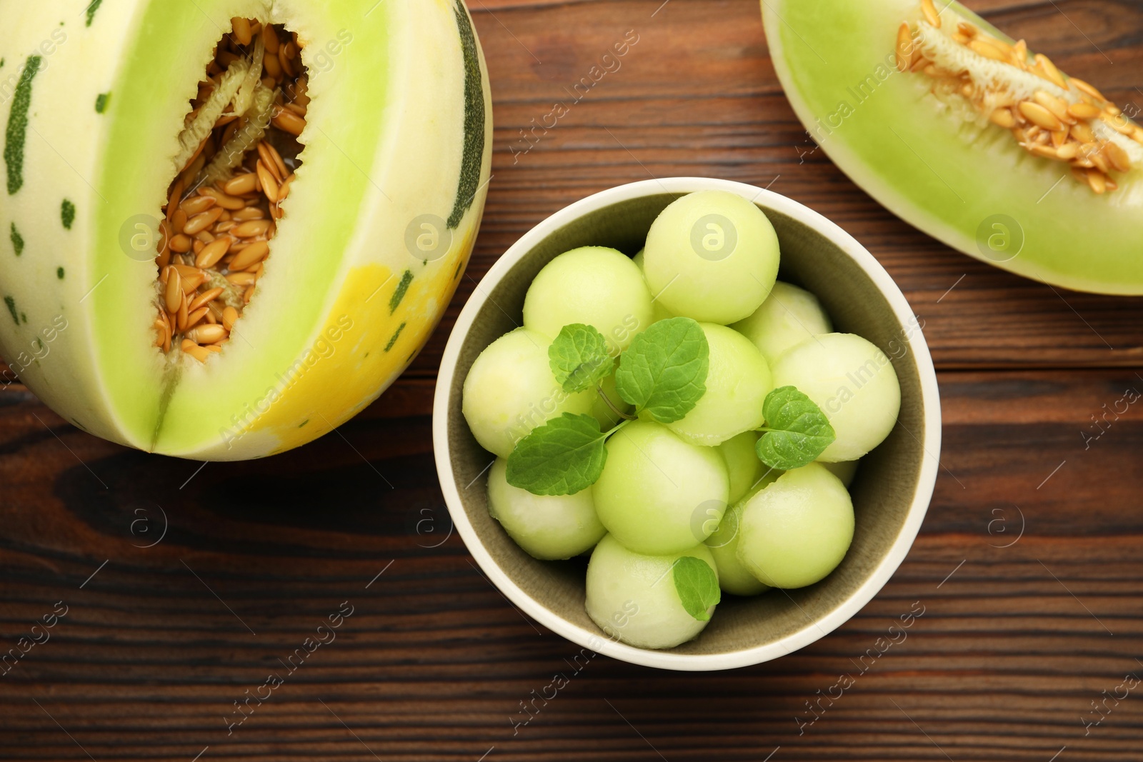 Photo of Melon balls in bowl and fresh fruit on wooden table, flat lay