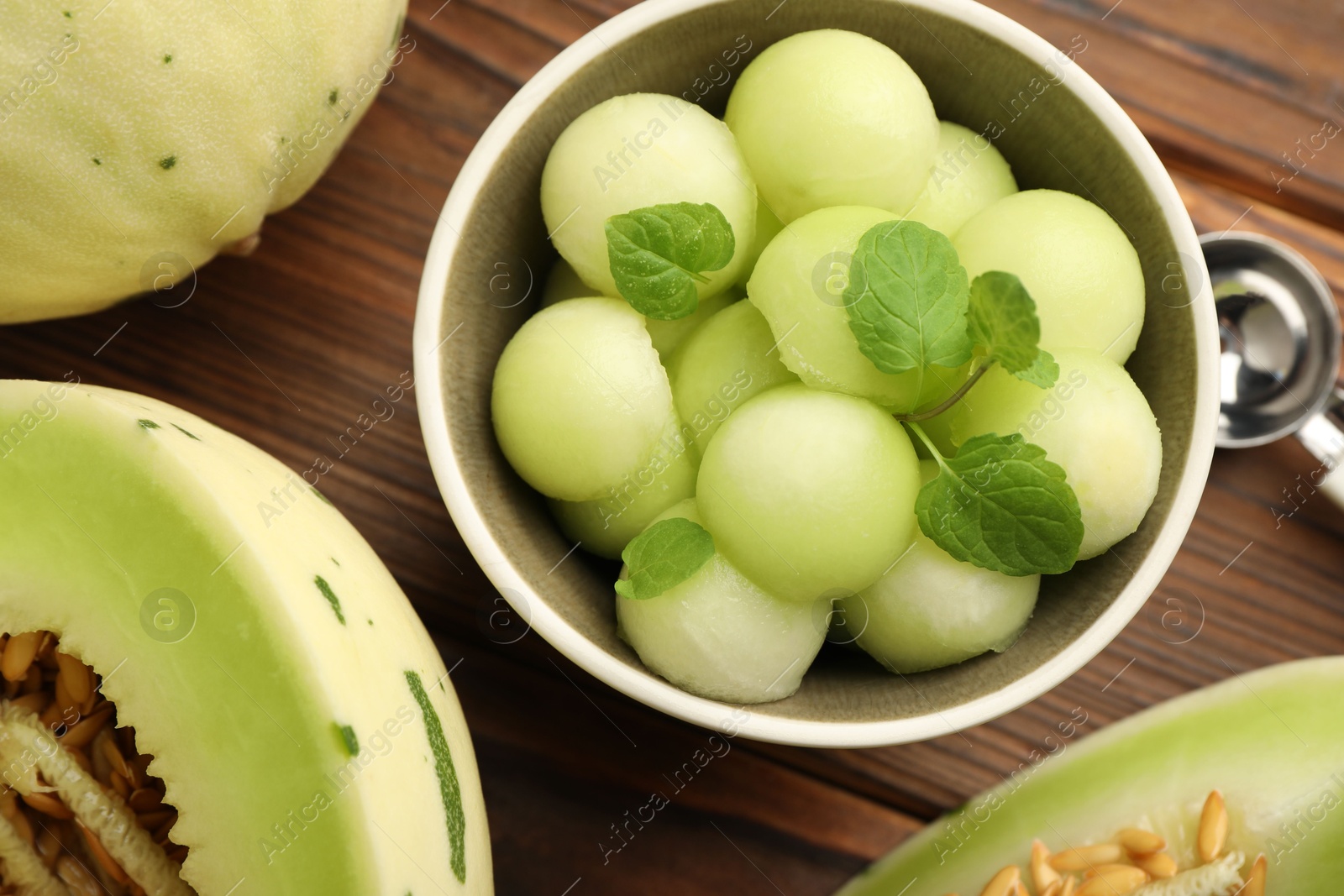 Photo of Melon balls in bowl and fresh fruit on wooden table, flat lay