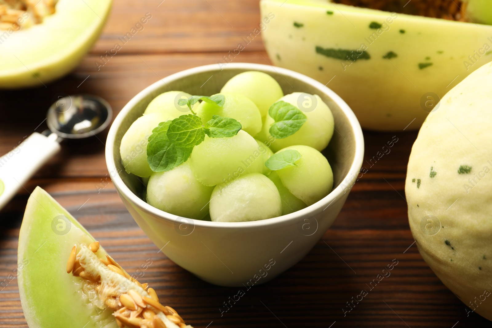 Photo of Melon balls in bowl and fresh fruit on wooden table, closeup