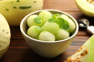 Photo of Melon balls in bowl and fresh fruit on wooden table, closeup