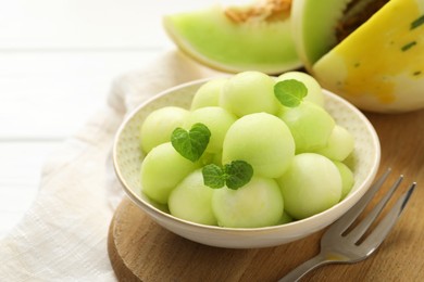 Photo of Melon balls in bowl and fresh fruit on white wooden table, closeup. Space for text