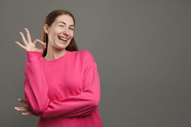 Photo of Smiling girl with braces showing ok gesture on grey background, space for text