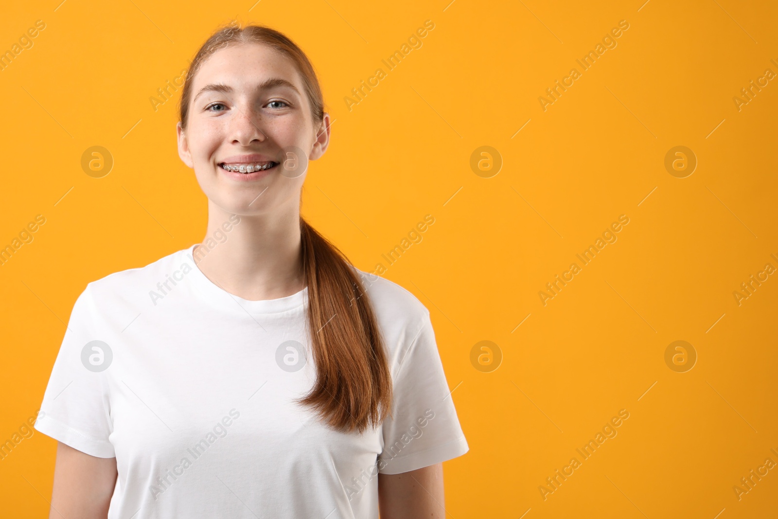 Photo of Smiling girl with braces on orange background, space for text