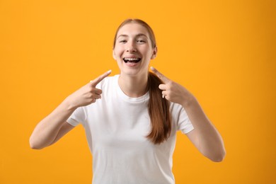 Photo of Girl pointing at her braces on orange background