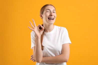 Photo of Smiling girl with braces showing ok gesture on orange background