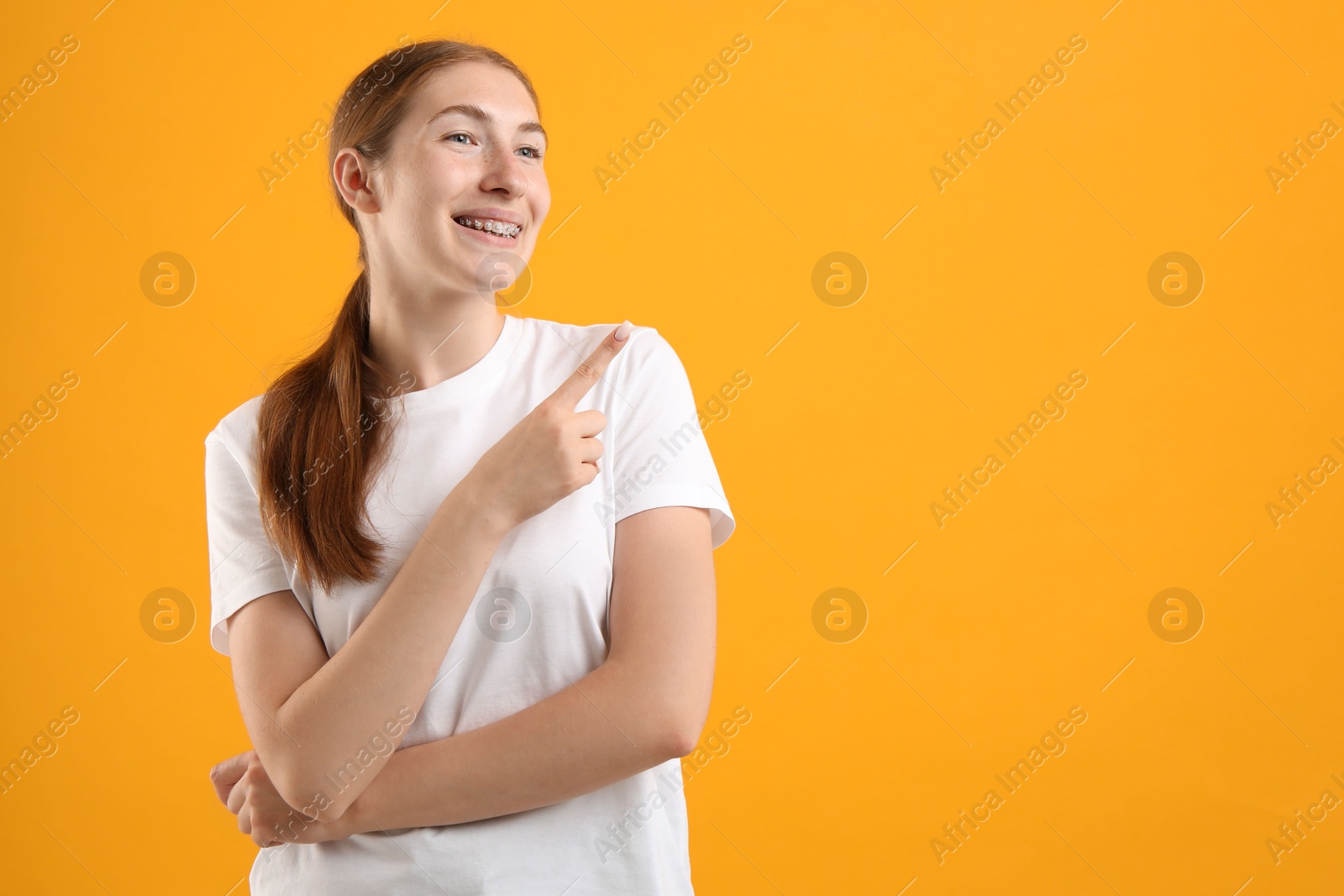 Photo of Smiling girl with braces on orange background, space for text